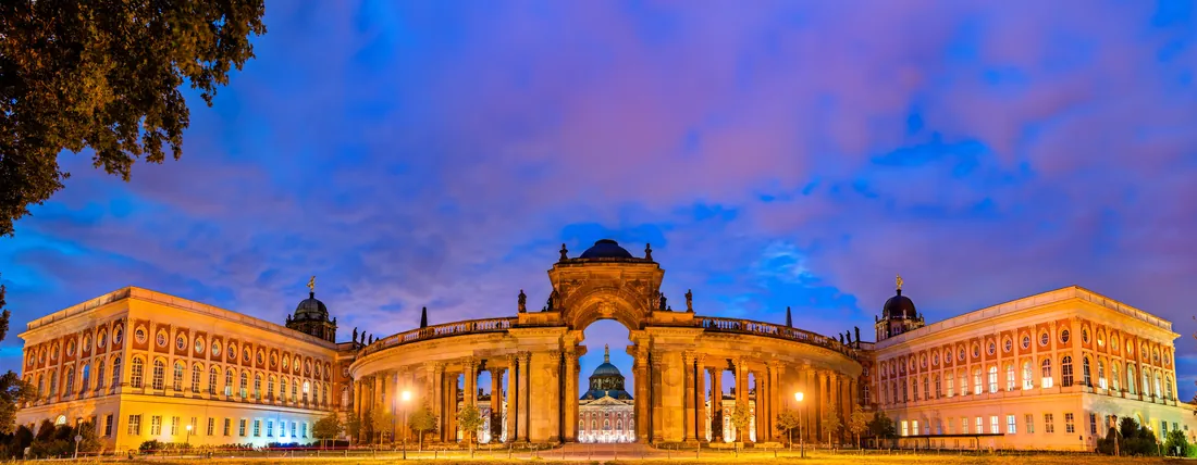 The illuminated colonnade of the New Palace at Sanssouci at dusk